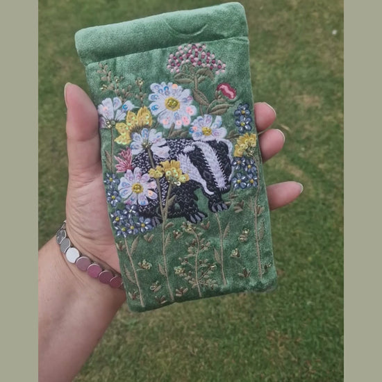 Green velvet glasses case decorated with an embroidered scene featuring a Badger in a flower garden. The scene is finished with beads and sequins.