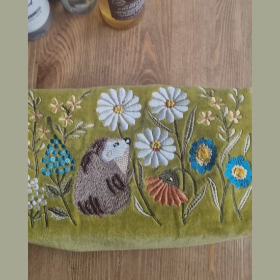 Video depicting velvet mustard coloured wash bag decorated with embroidered flower garden design being loaded with toiletries.