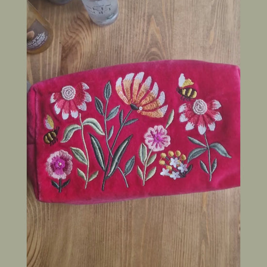 Video depicting velvet pink wash bag decorated with embroidered flower garden design being loaded with toiletries.