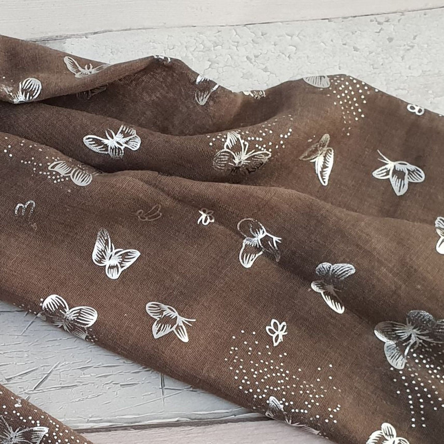 Close up Photo of khaki coloured scarf covered in metallic Silver butterflies