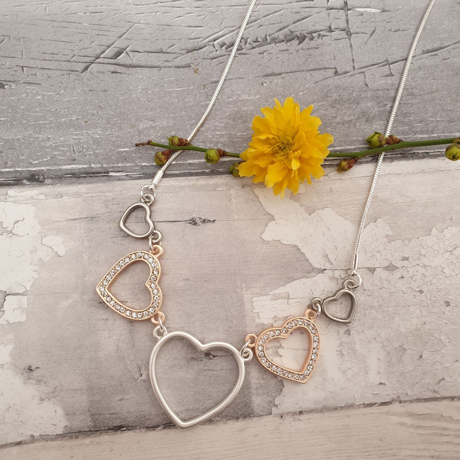 Photo of a necklace comprising rose, silver and pewter coloured love hearts on a silver chain
