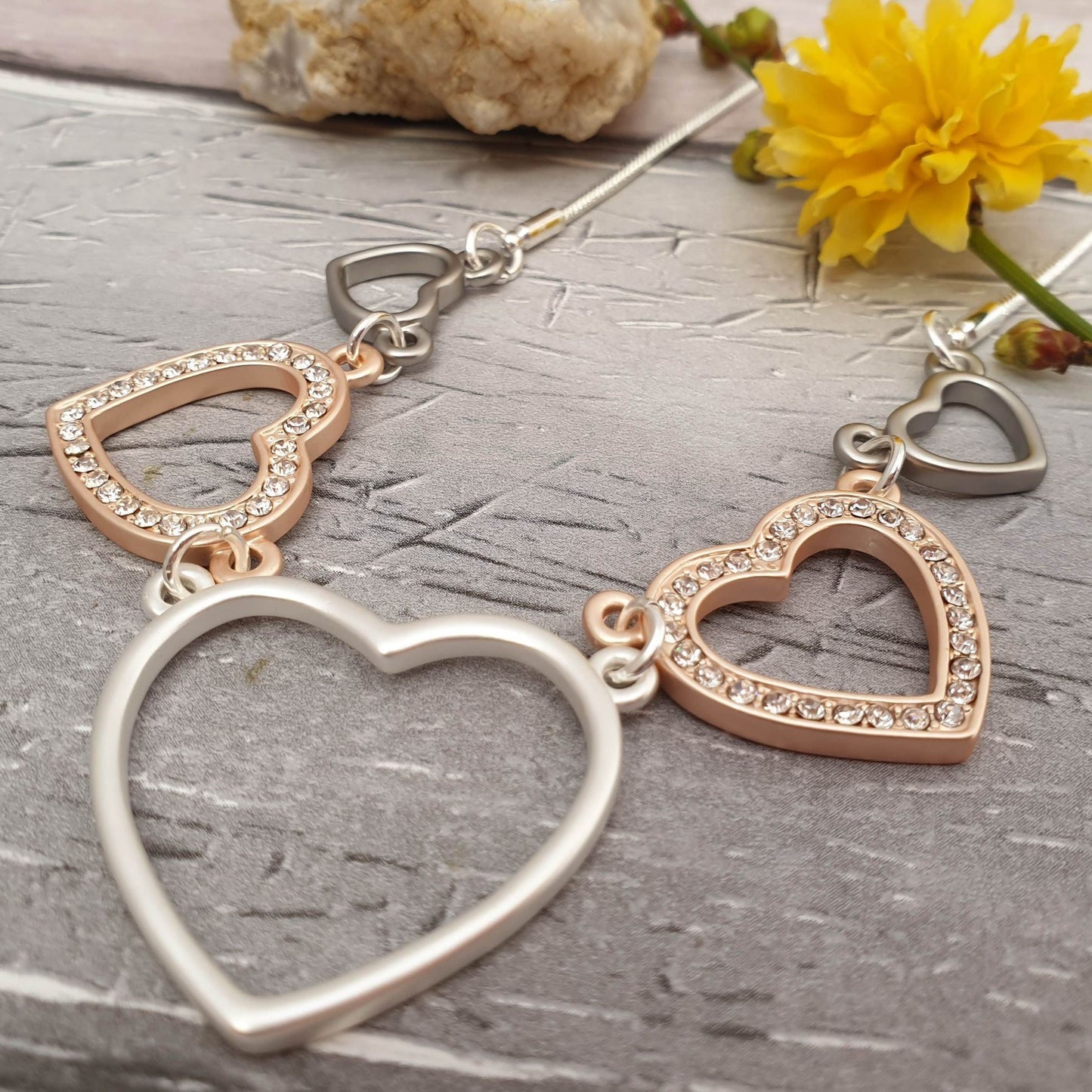 Photo of a necklace comprising rose, silver and pewter coloured love hearts on a silver chain