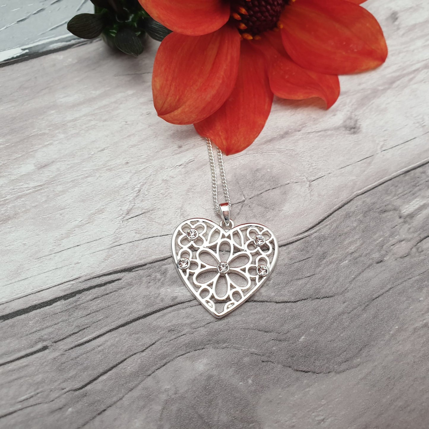 Photo of a silver heart shaped pendant with tiny silver daisys