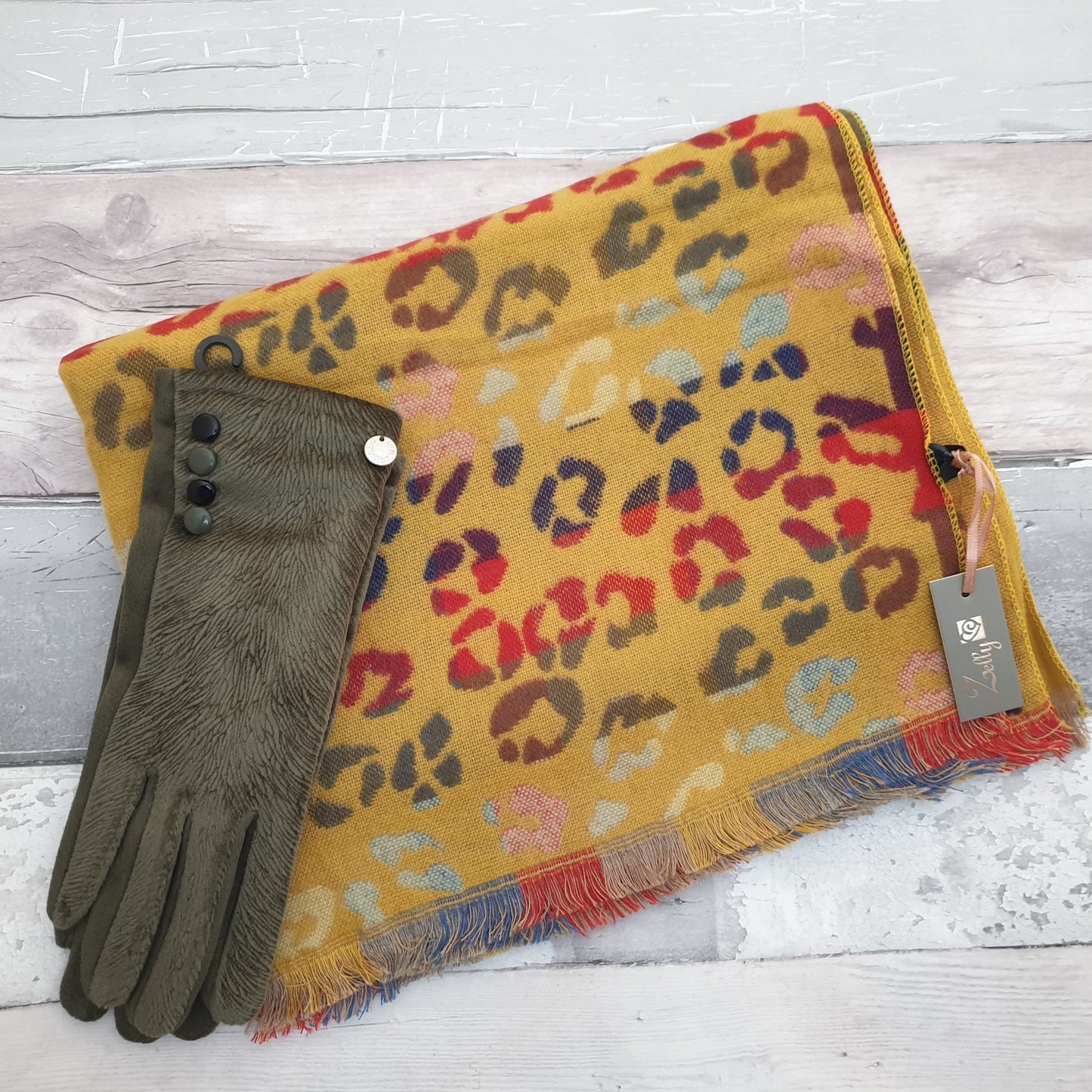 Photo of a mustard coloured animal print scarf with rainbow colours and a pair of matching olive green coloured gloves