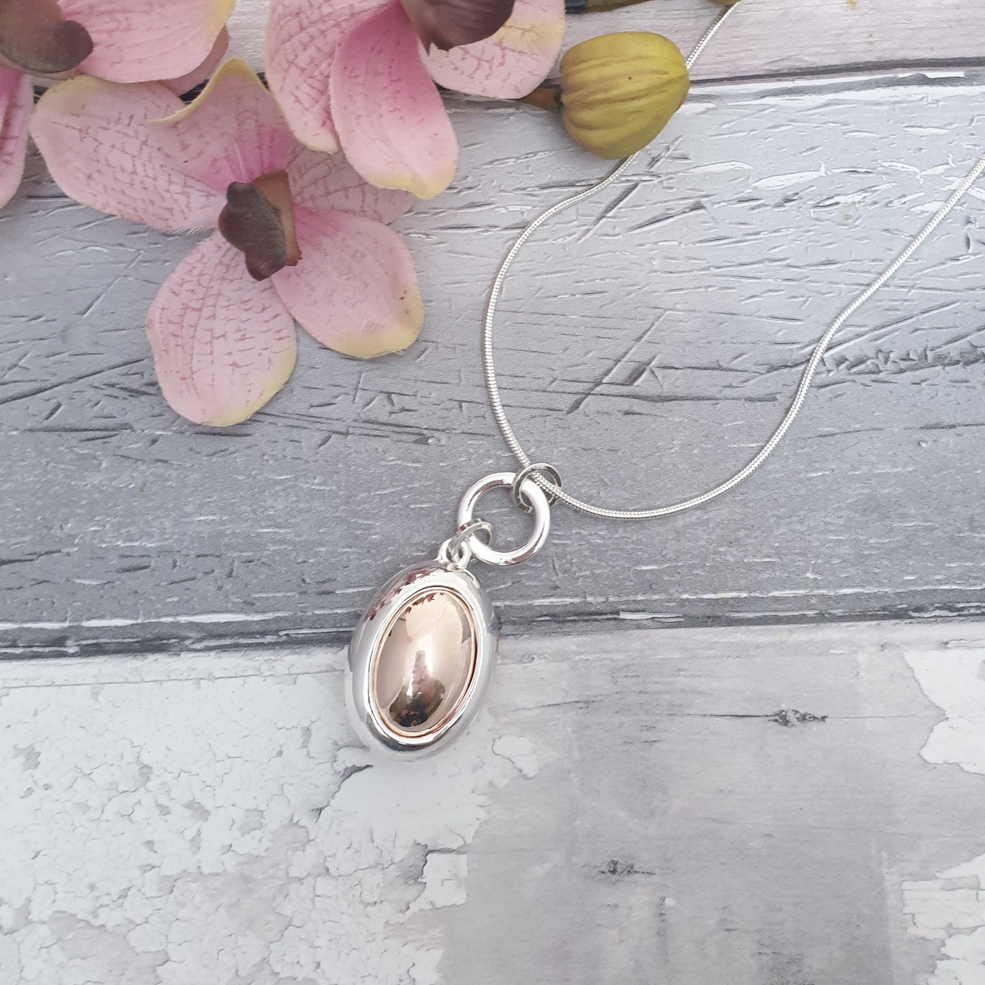 Photo of a long length necklace with an oval pendant in rose gold and silver colourings