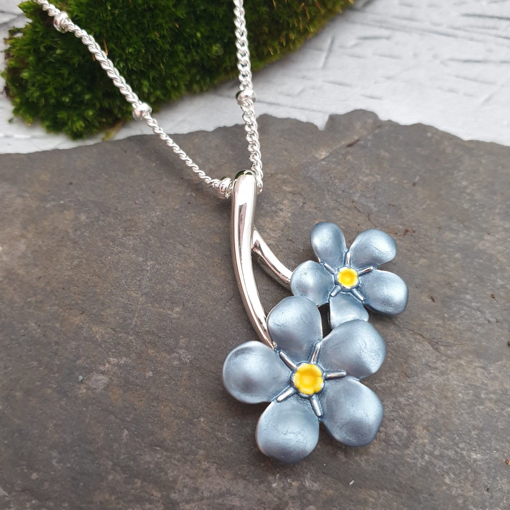 Photo of a double forget-me-not flower on a curb silver coloured chain