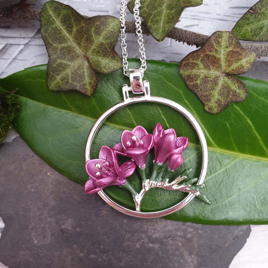 Photo of a spray of deep pink freesia flowers within a circular surround to form a pendant