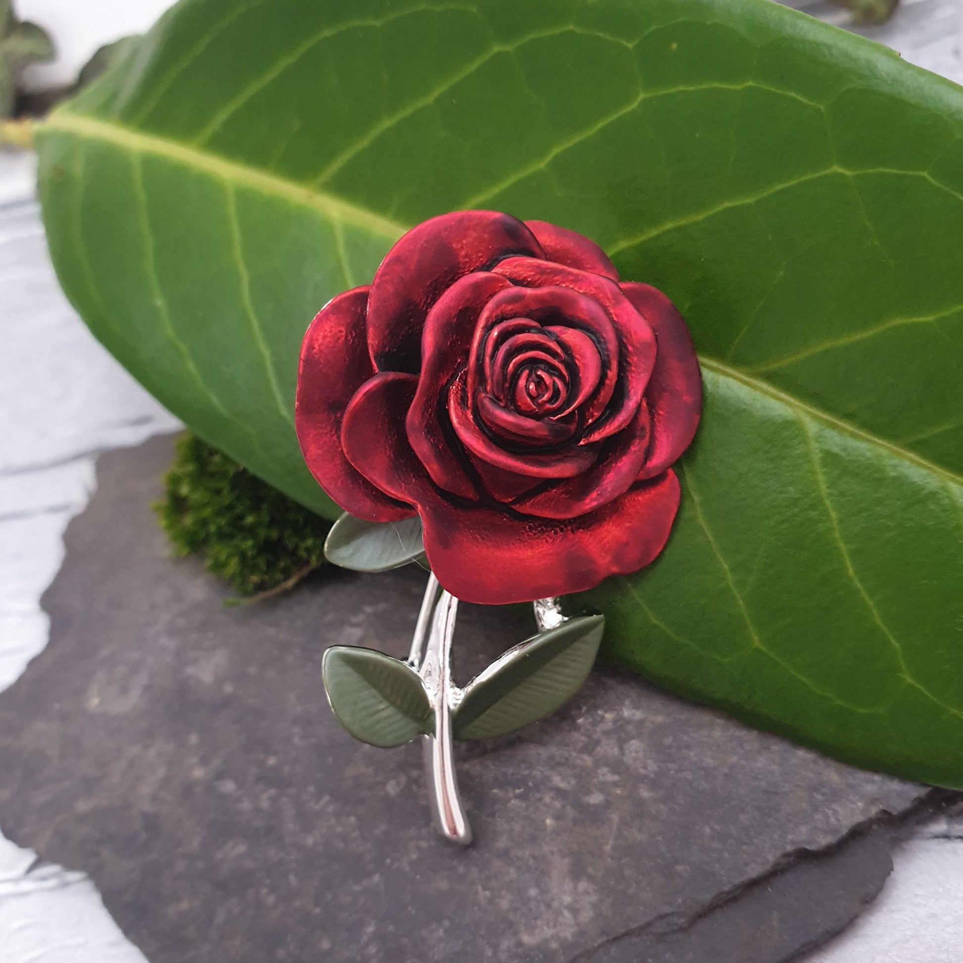 Photo of a single red rose with a silver stem and green leaves as a ladies brooch