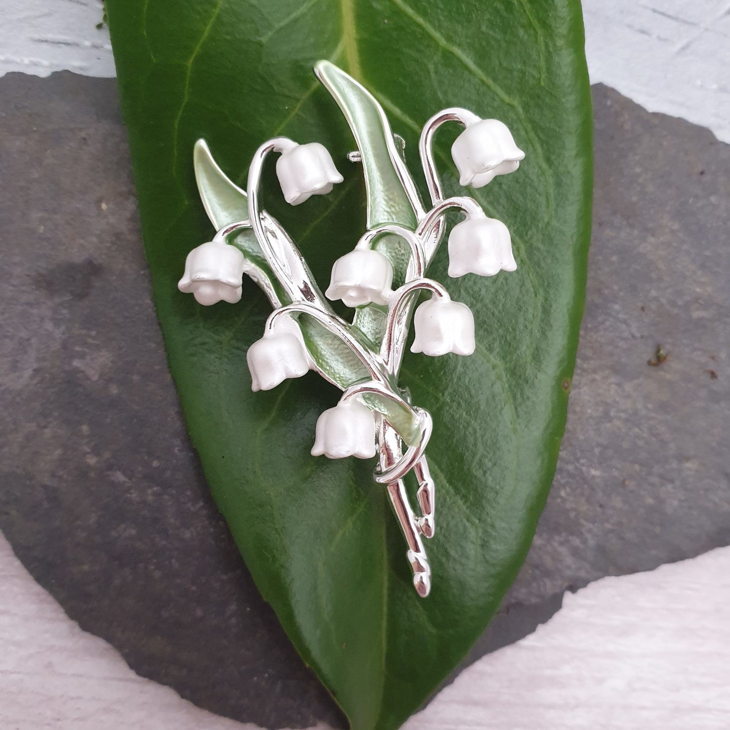 Photo of a spray of Lily of the Valley white flowers and green leaves formed as a ladies brooch with a silver stem