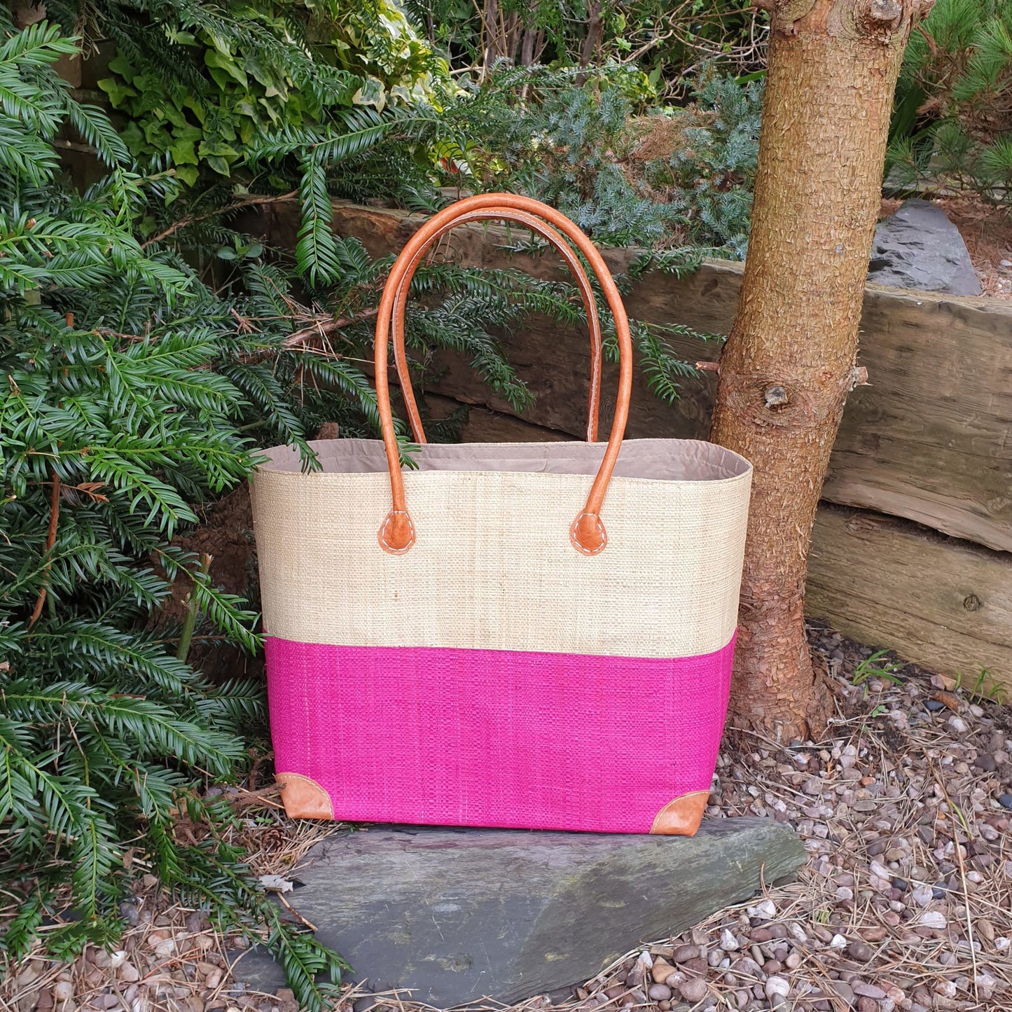 Photo of a large two tone pink raffia basket with drawstring top and leather handles