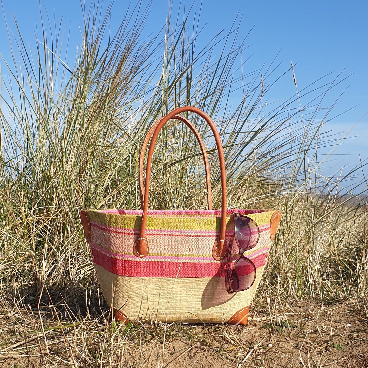 Photo of a small bato style basket with pink and lime stripes. Leather handles