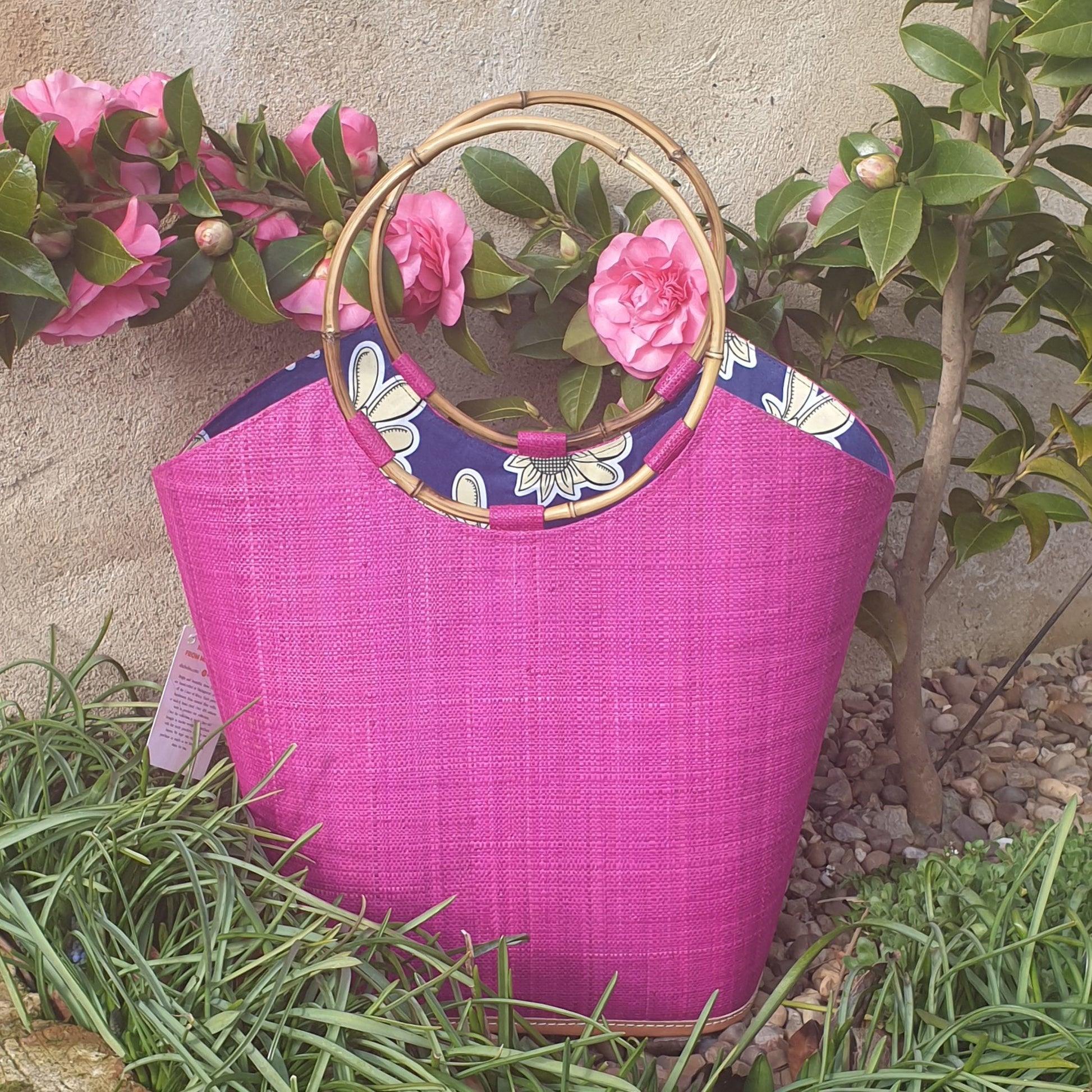Photo of a finely woven raffia basket in shocking fuschia pink with a circular rigid bamboo handle