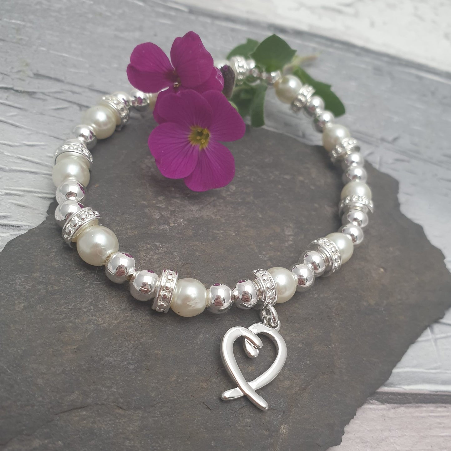 A silver and pearl stretch bracelet with diamante covered spacers. The bracelet has a silver love heart charm attached to one of the spacers.
