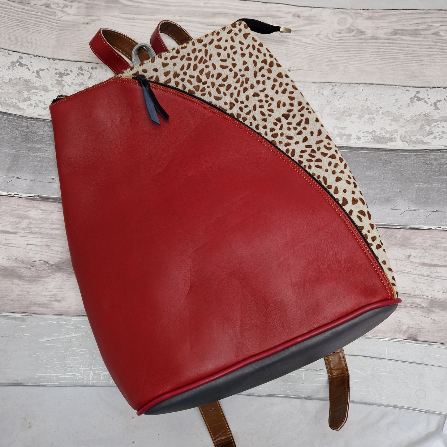 Red leather backback with white cow hide panel decorated in brown spots.