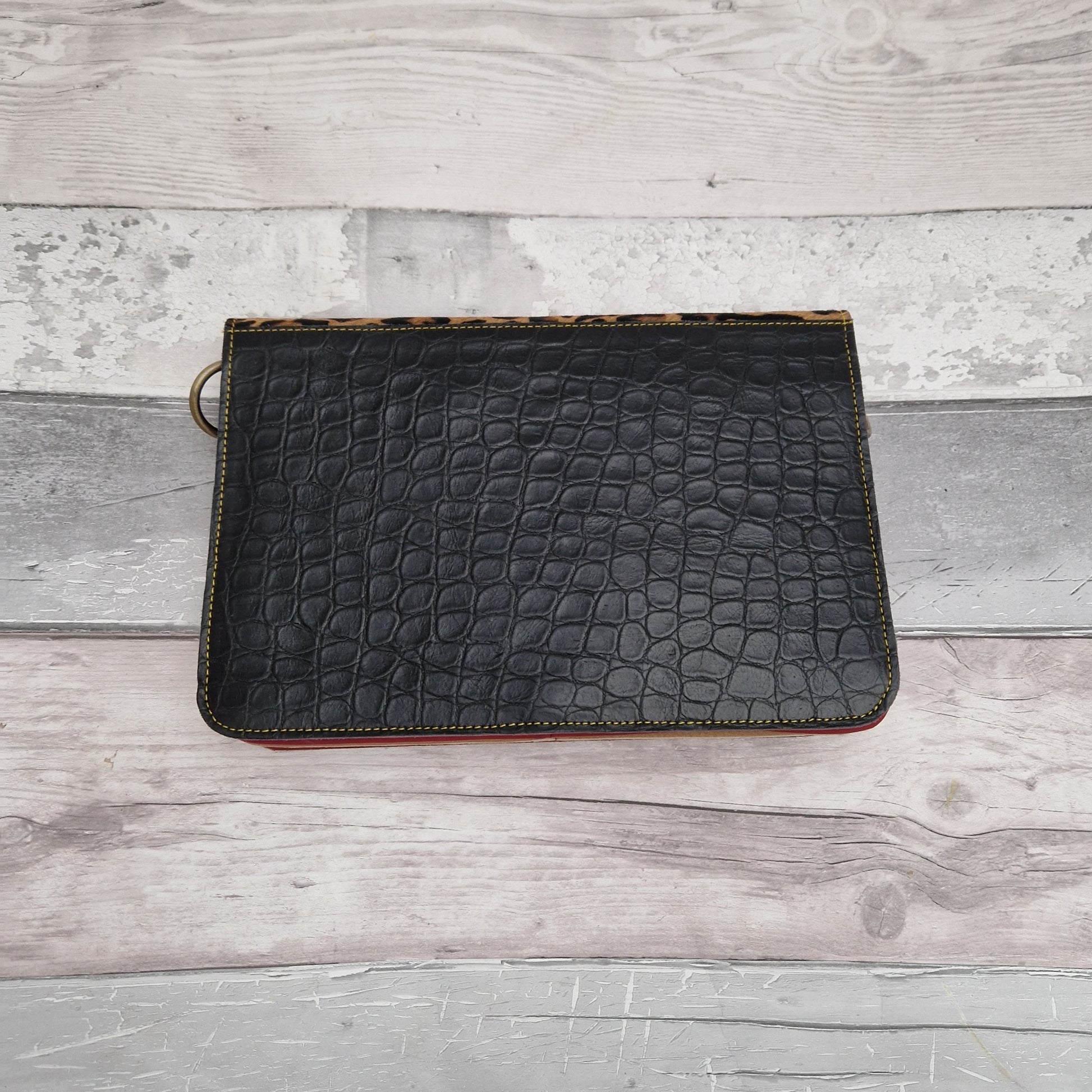 Black leather handbag with a textured leopard print panel.