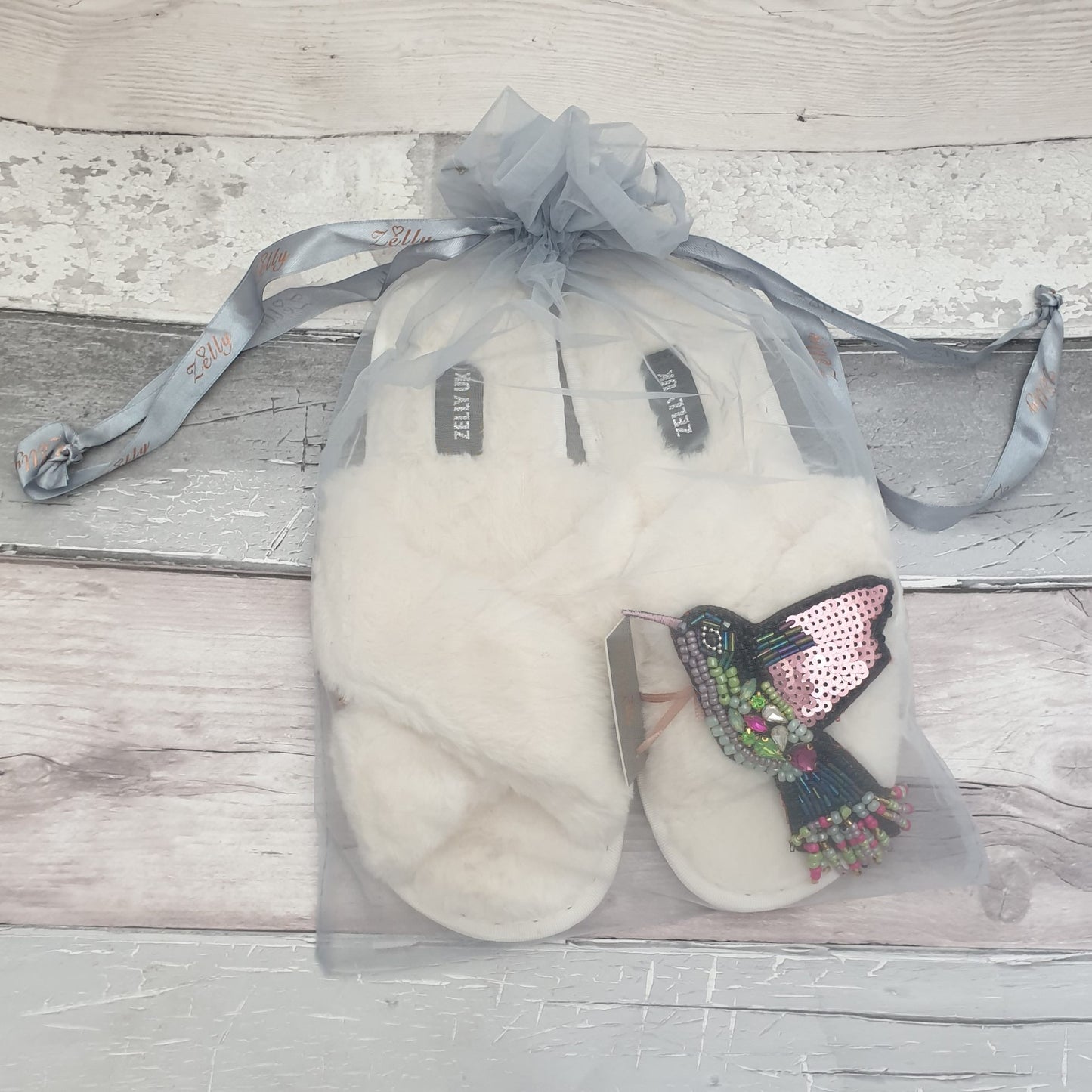 White fluffy slippers with a Hummingbird brooch in a grey organza bag