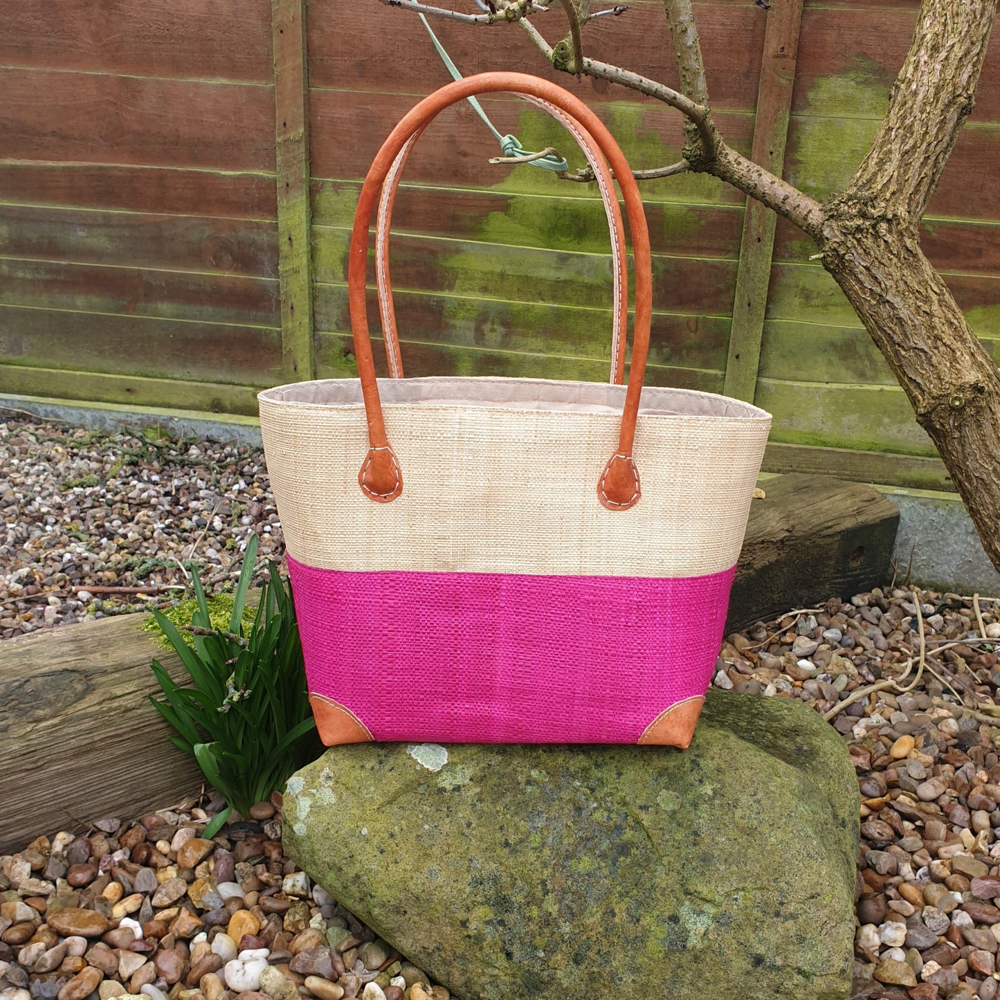 Photo of a small two tone pink raffia basket with drawstring top and leather handles
